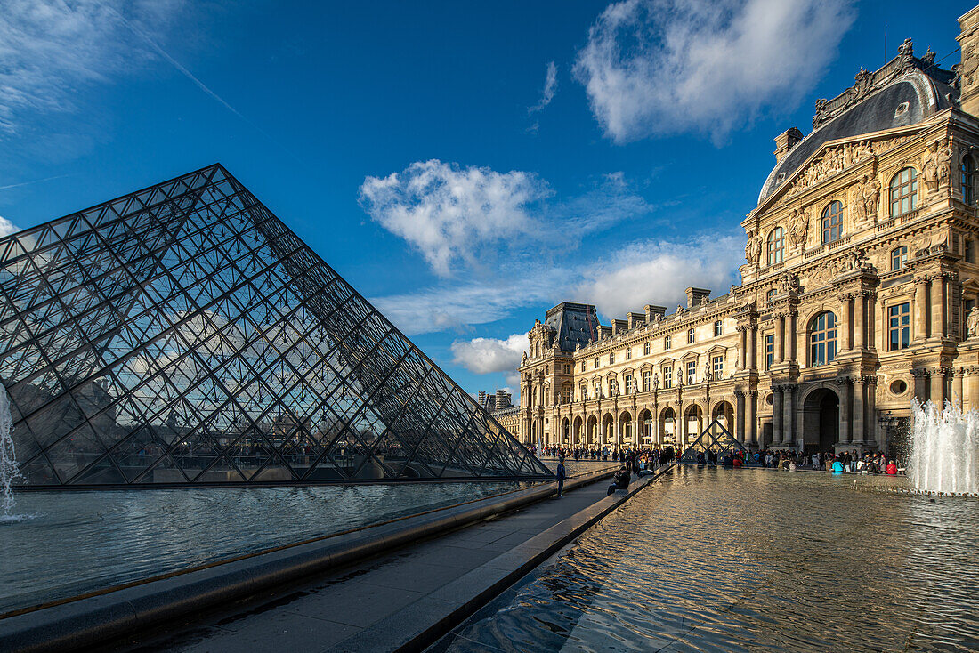 Besucher spazieren in der Nähe des Palais Royal unter einem klaren blauen Himmel.