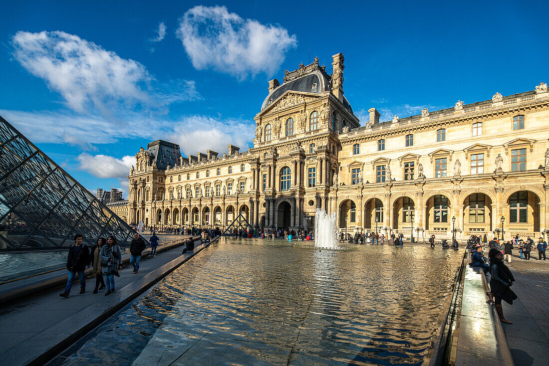 Besucher spazieren in der Nähe des Palais Royal unter einem klaren blauen Himmel.