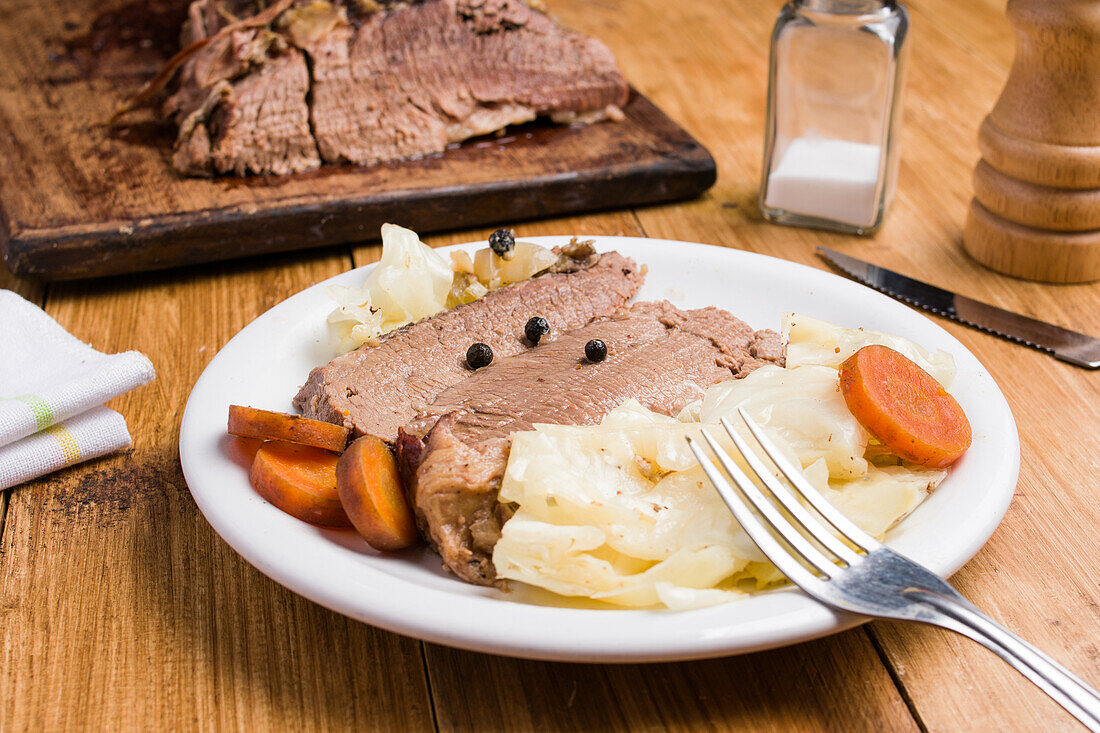 Leckeres hausgemachtes Corned Meat mit Kohlstücken und Karotten auf einem Teller auf einem Holztisch serviert