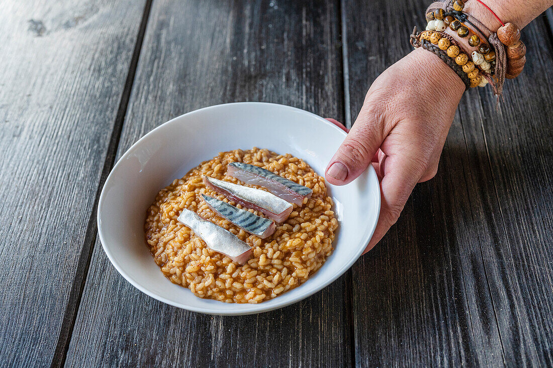 Blick von oben auf einen Mann mit Armbändern, der eine Schüssel mit leckerem Reis und Fisch auf einen Holztisch stellt