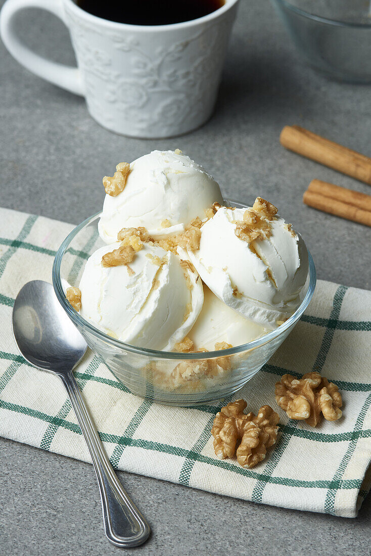 Leckeres hausgemachtes Gelato mit Walnüssen, serviert in einer Glasschale auf einem Tisch mit einer Tasse Kaffee und Zimtstangen in der Küche