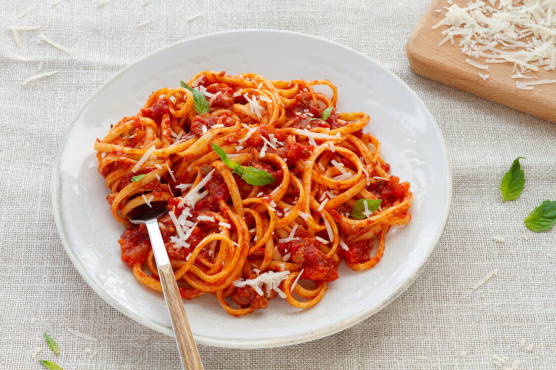 Blick von oben auf appetitliche hausgemachte Pasta mit Bolognesesoße, serviert mit frischen Basilikumblättern auf einem weißen Teller