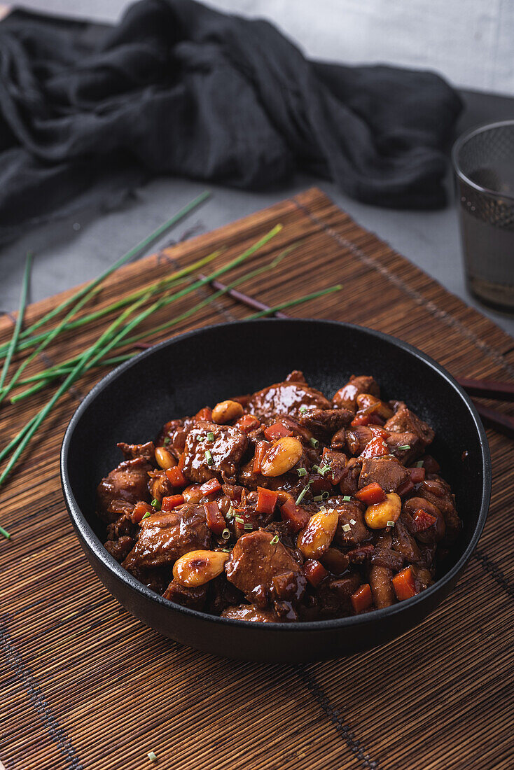 Schale mit asiatischem Hähnchenfleisch mit Mandeln und Gemüse in der Nähe von Bambus-Essstäbchen und Schnittlauch von oben