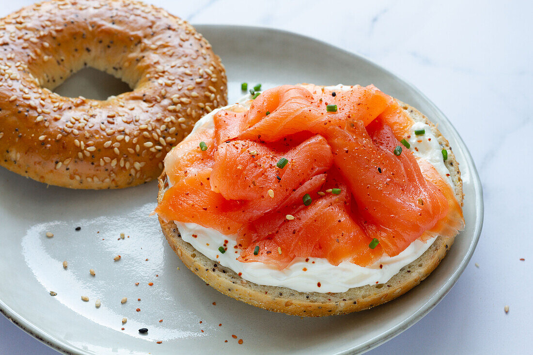 Von oben frischer Bagel mit Käse und Lachs auf einem Teller, serviert auf einem Tisch in einer hellen Küche