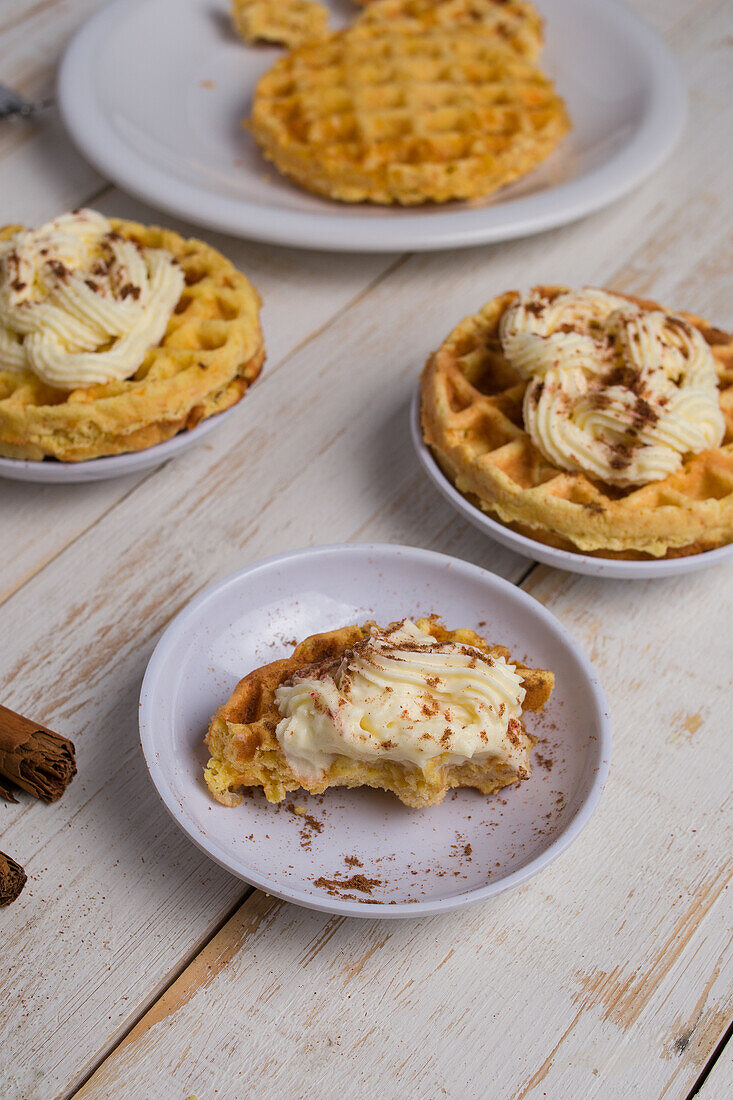 Von oben von frisch gebackenen hausgemachten Kürbis-Käse-Waffeln mit Zuckerguss auf Holztisch mit Zimtstangen in hellen Küche platziert