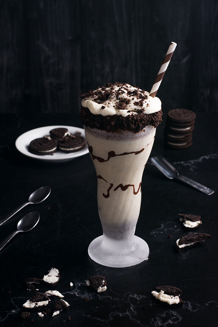 Blick von oben auf leckeren Milchshake mit zerstoßenen Keksen und Strohhalm im Glas mit Schokoladensoße