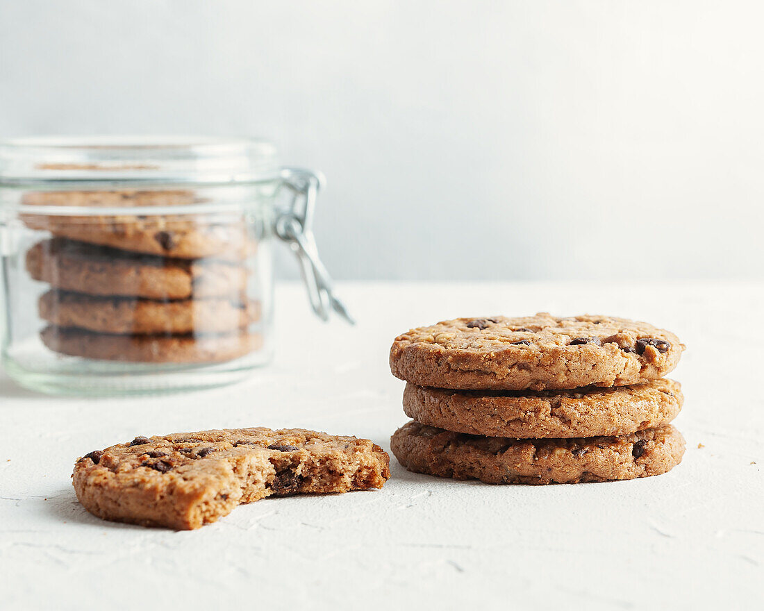 Abundance of delicious sweet cookies with chocolate chips placed on white table with glass jar on white background in light kitchen