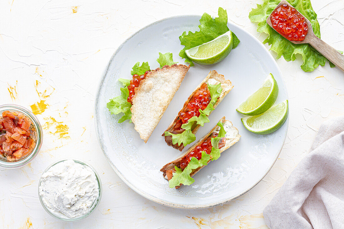 Kleine leckere Tacos mit rotem Kaviar und grünem Salat, serviert auf einem hölzernen Schneidebrett auf dem Tisch