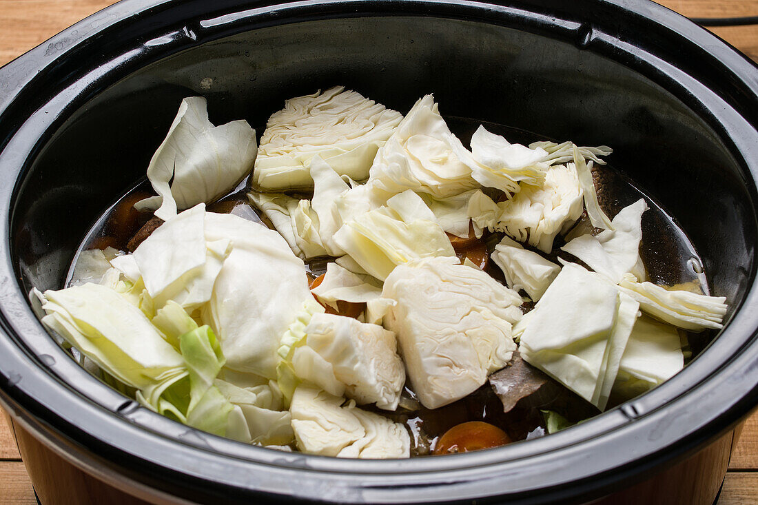 Von oben gesehen kochen geschnittene Kohl- und Gemüsestücke im Langsamkocher bei der Vorbereitung für Corned Beef