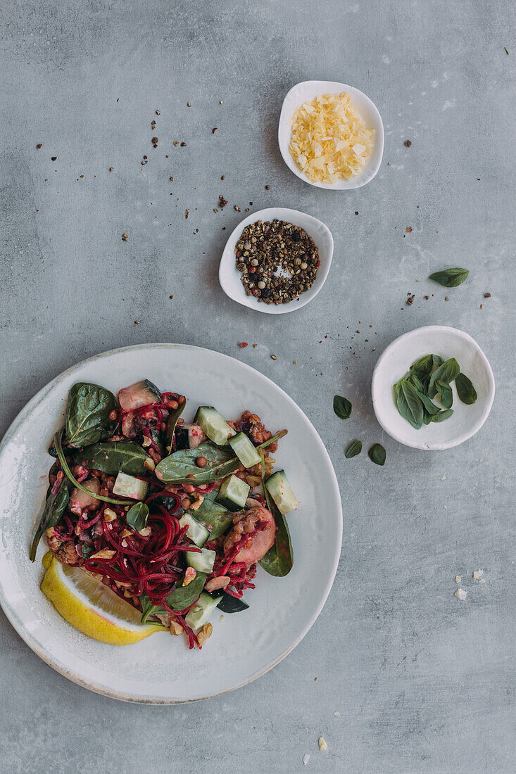 Draufsicht auf Teller und Schale mit leckerem Linsensalat mit Gurken und Spinat neben Servietten auf grauem Tisch