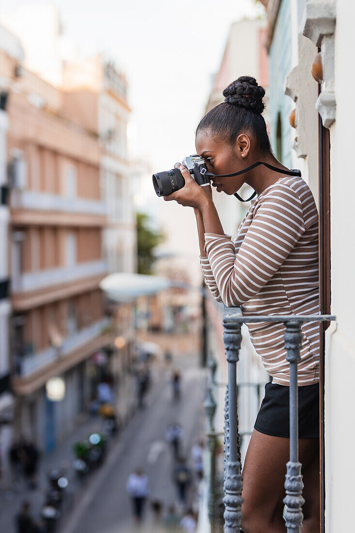 Seitenansicht ethnische Frau in Kleidung mit gestreiftem Ornament mit professionellem Fotogerät auf dem Balkon bei Tageslicht