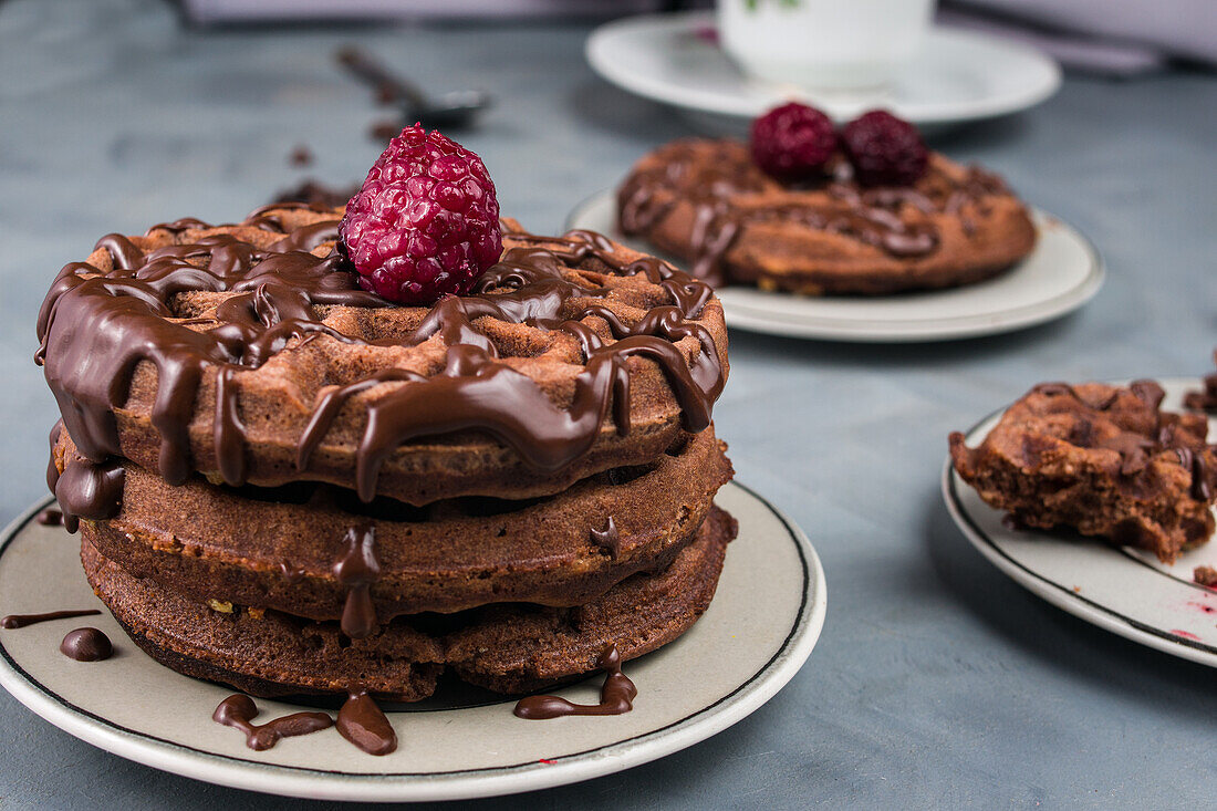 Leckere süße Waffeln mit Schokoladensauce und Himbeeren auf einem Tisch in einer hellen Küche