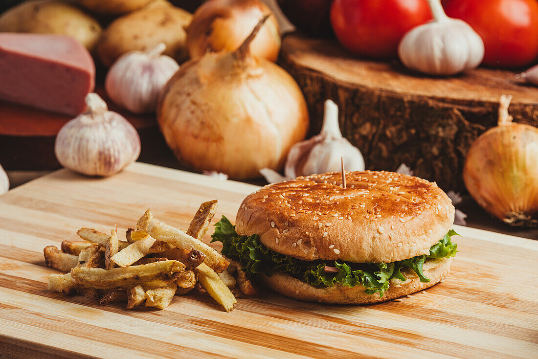 Appetitliche Hamburger mit Gemüse auf Holzbrett mit Pommes frites in Küche