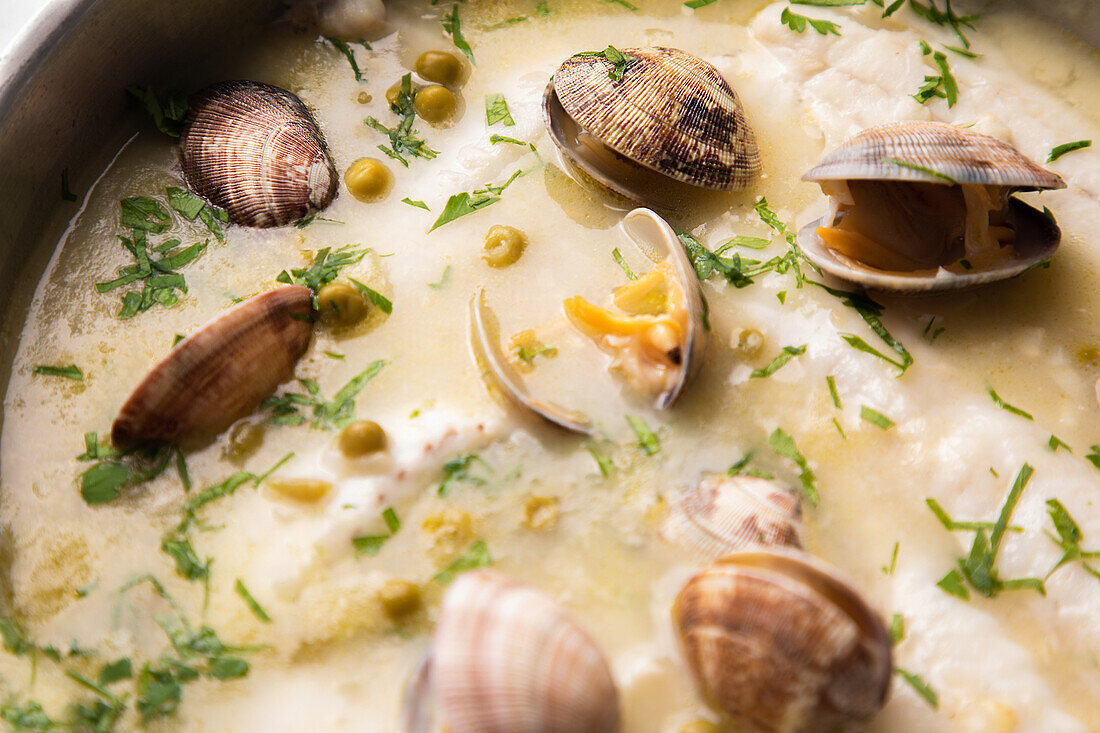 From above metal saucepan with delicious seafood soup with clams and hake