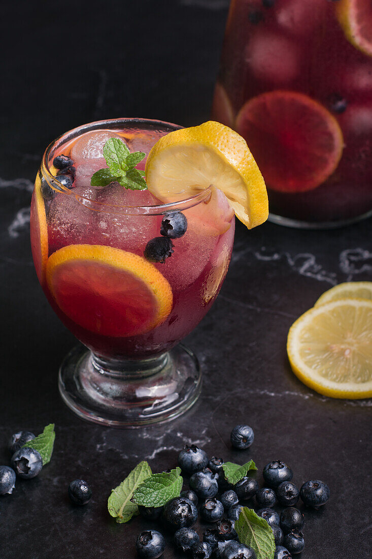 Hoher Winkel von Glas und Krug mit erfrischender kalter Limonade mit frischen Blaubeeren und Zitronenscheiben auf einem dunklen Tisch