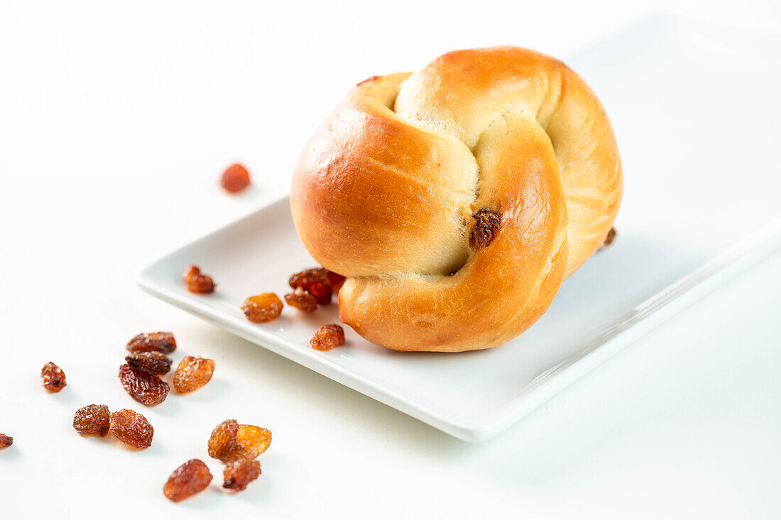 Von oben köstliches gedrehtes Brötchen mit süßen Rosinen auf rechteckigem Teller auf weißem Hintergrund