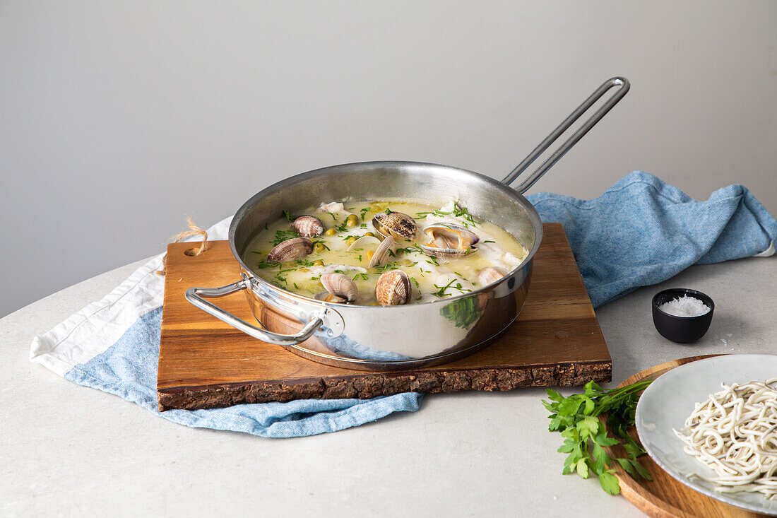 Von oben Metalltopf mit köstlicher Meeresfrüchtesuppe mit Venusmuscheln und Seehecht auf einem Holzbrett in der Küche