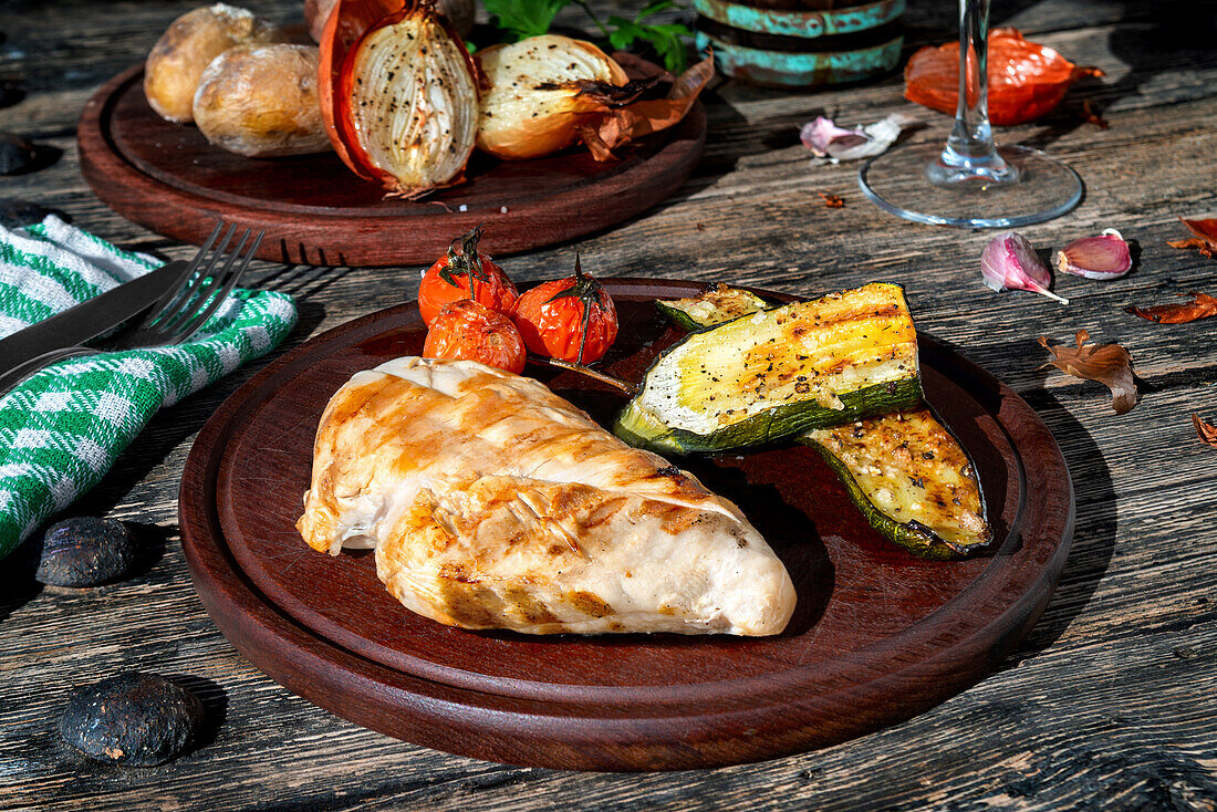 Leckere gegrillte Hühnerbrust auf Teller mit frischen gerösteten Kirschtomaten und Zucchini auf Holztisch mit Zwiebel