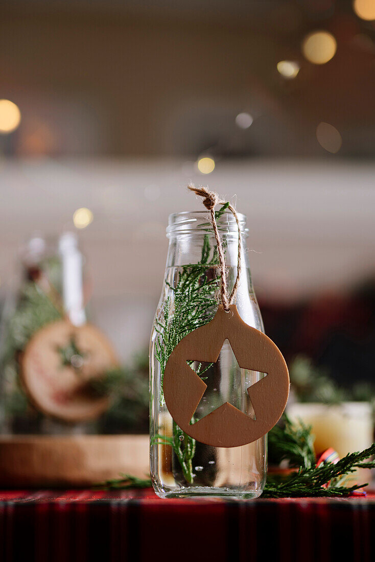 Weihnachtlich gedeckter Tisch mit Kranz und dekorativen Holzornamenten und rot karierter Tischdecke mit gelben Lichtern im Hintergrund