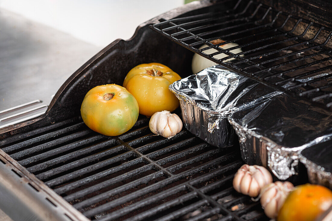 Nahaufnahme rohe Scheiben frischer Tomaten und Knoblauchköpfe beim Grillen auf einem Metallrost