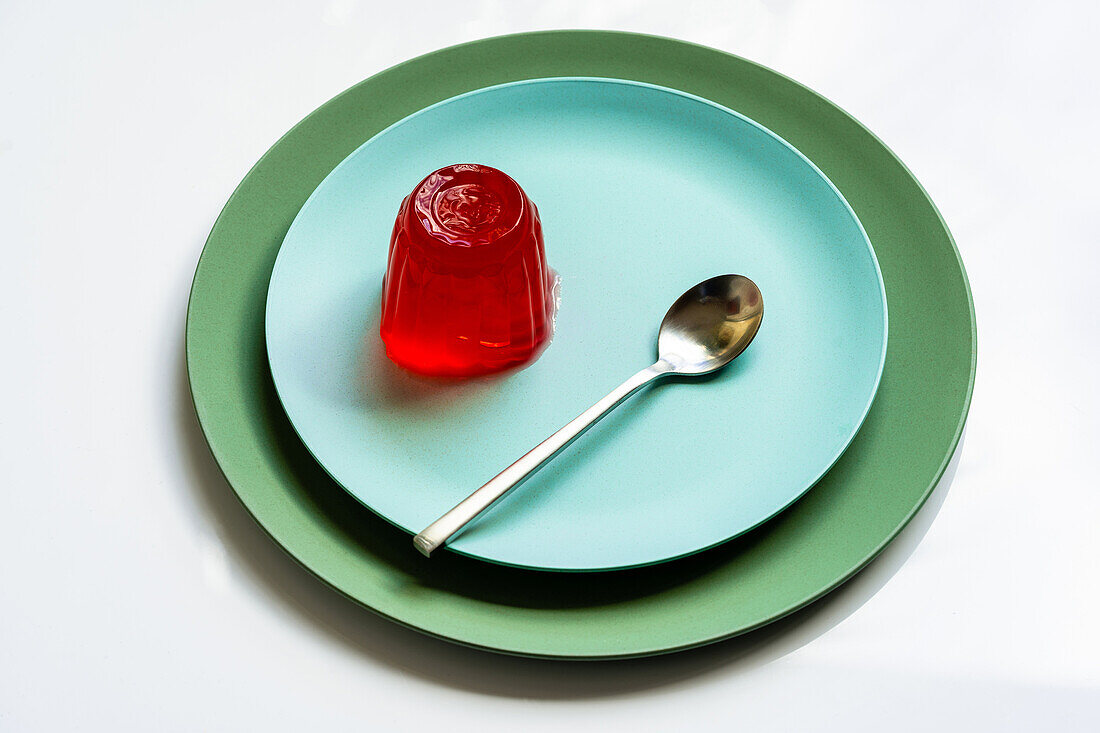 From above of appetizing red berry jelly placed on pale blue round plate with spoon on white surface