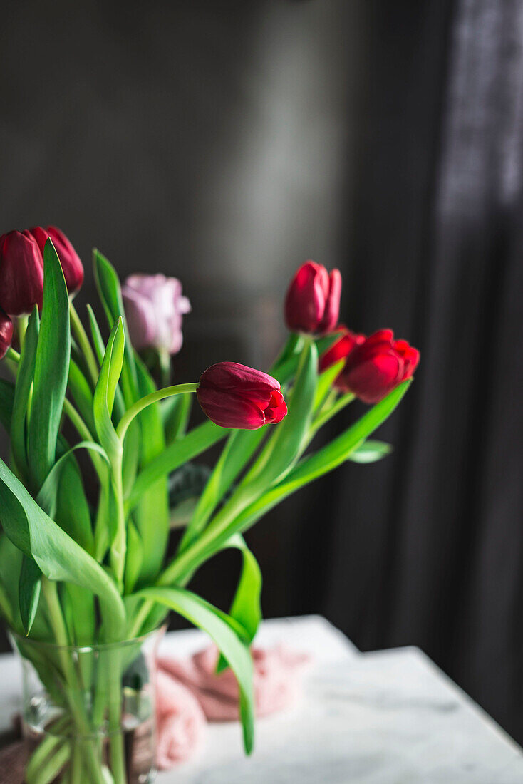 Glasvase mit roten Tulpen auf dem Tisch am Fenster