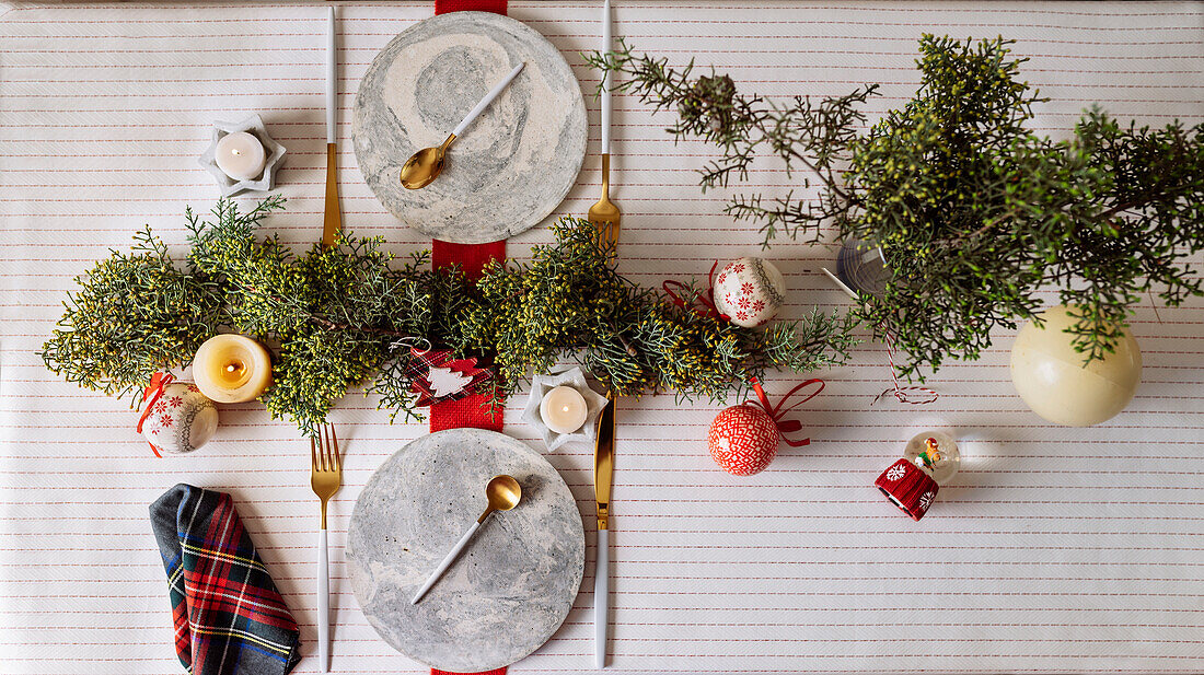 Von oben auf einen weihnachtlich gedeckten Tisch mit Kranzdekoration, rot und weiß, mit goldenem Besteck und Kerzen