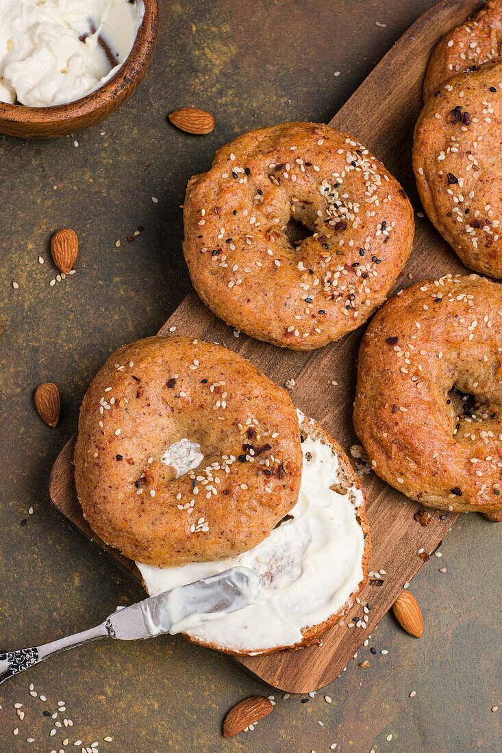 Leckere gebackene kohlenhydratarme Bagels auf einem Holzbrett auf einem Tisch mit Mandeln und Frischkäse in einer hellen Küche