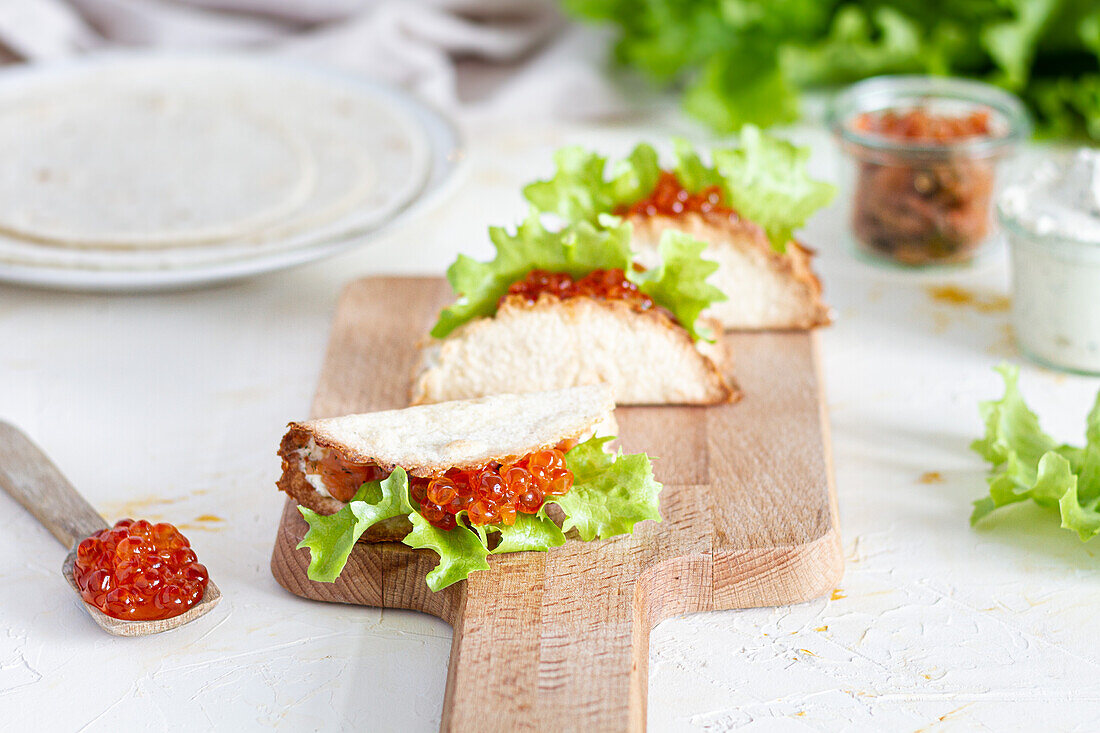 Kleine leckere Tacos mit rotem Kaviar und grünem Salat, serviert auf einem hölzernen Schneidebrett auf dem Tisch