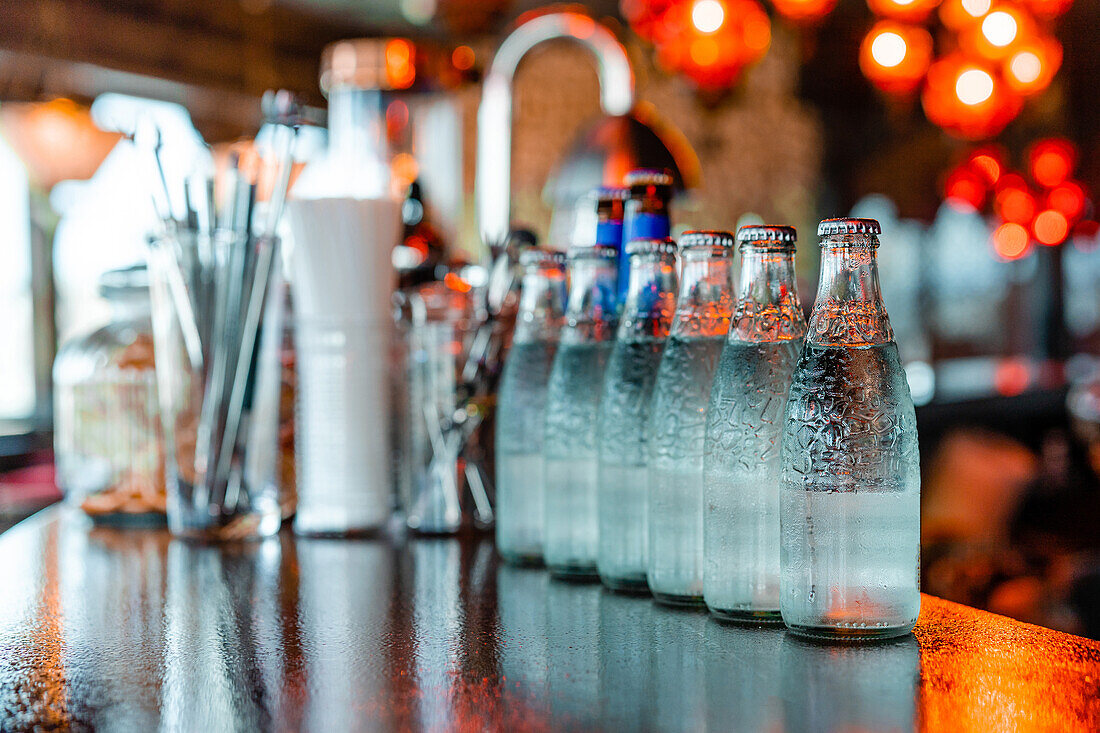 Glasflaschen mit kaltem, erfrischendem Wasser stehen in einer Reihe auf einem Holztresen in einer Bar