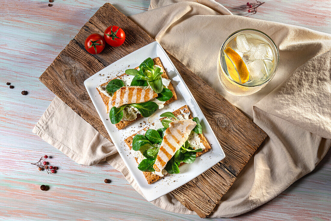 Draufsicht auf leckere Toasts mit gegrilltem Hähnchenfilet und Blattspinat, serviert auf einem Schneidebrett aus Holz neben einem Erfrischungsgetränk