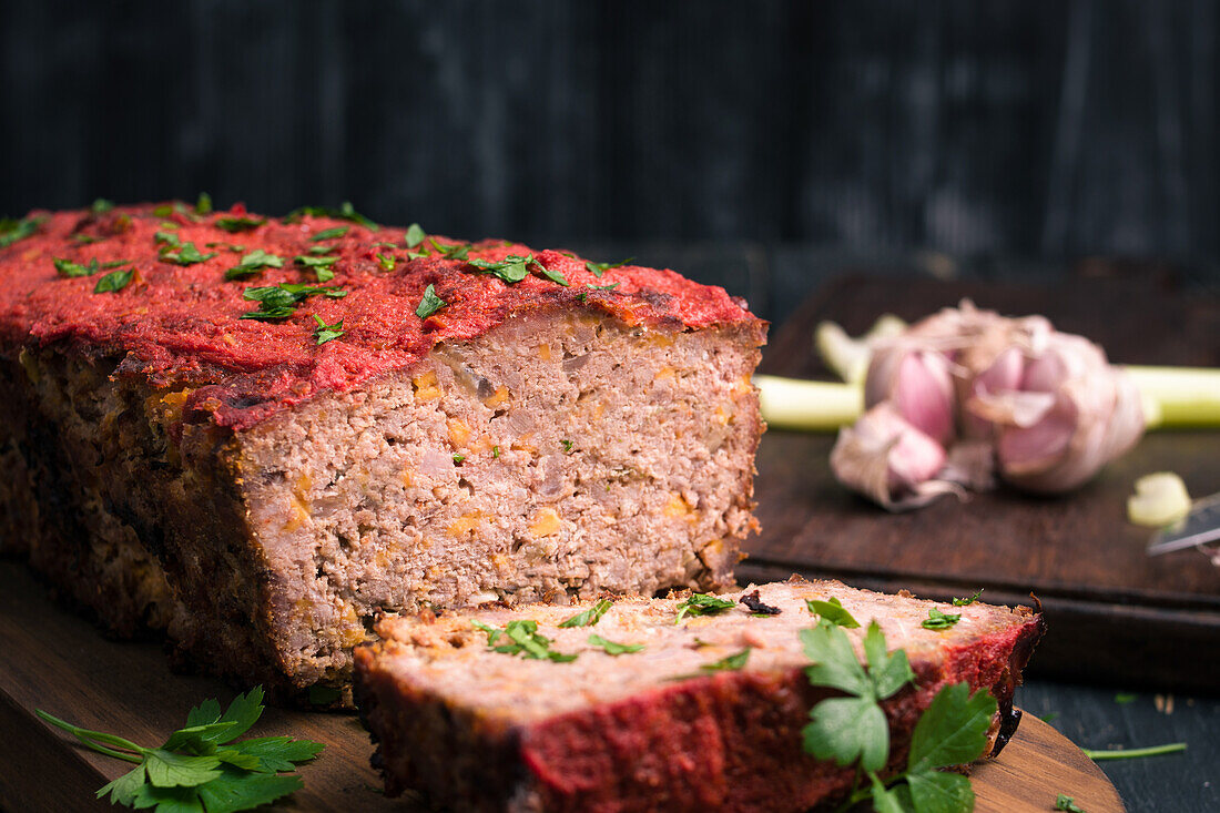 Leckerer hausgemachter Hackbraten mit Karotten und frischer grüner Petersilie auf einem hölzernen Schneidebrett auf dem Tisch