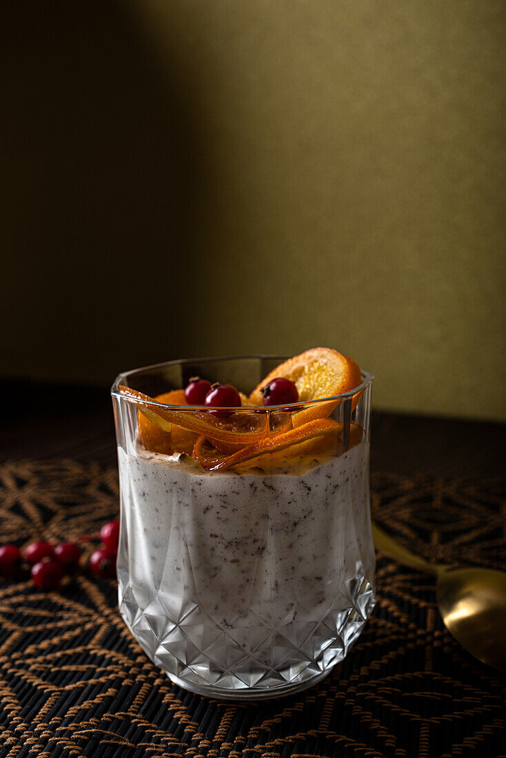 Glas mit Dessert aus Stracciatella-Mousse und Schokoladenspänen, gekrönt mit karamellisierten Orangenscheiben und Beeren neben dem Löffel