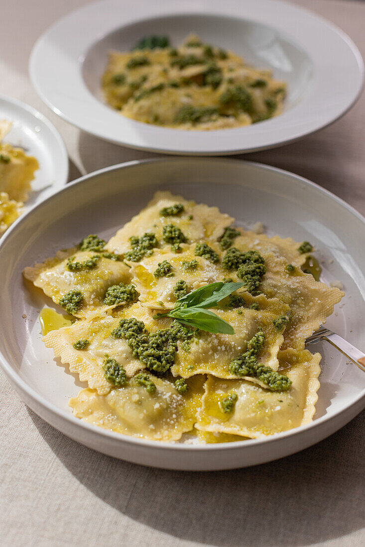 Von oben appetitlich gekochte Ravioli-Nudeln mit grüner Soße und Kräutern auf weißen Tellern mit Gabeln auf dem Tisch platziert