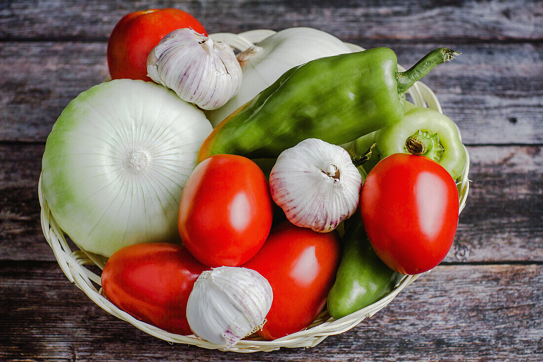 Frische reife Tomaten neben Paprika und Knoblauch in einer Schüssel auf einem Holztisch zu Hause