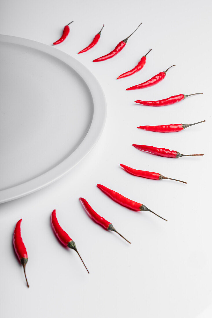 High angle composition of hot red chili peppers arranged around plate against white background