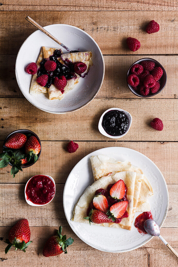 Von oben Teller mit leckeren Crêpes mit verschiedenen Belägen, die beim Frühstück auf einem Holztisch stehen