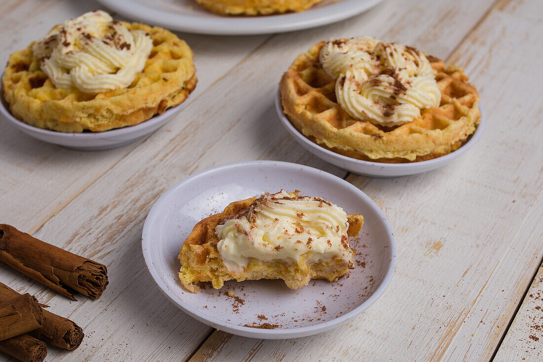 Von oben von frisch gebackenen hausgemachten Kürbis-Käse-Waffeln mit Zuckerguss auf Holztisch mit Zimtstangen in hellen Küche platziert