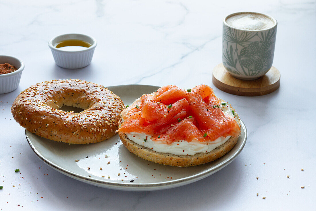 Frischer Bagel mit Käse und Lachs auf einem Teller, serviert auf einem Tisch mit einer Tasse heißem Kaffee in einer hellen Küche