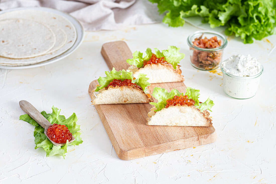 Kleine leckere Tacos mit rotem Kaviar und grünem Salat, serviert auf einem hölzernen Schneidebrett auf dem Tisch