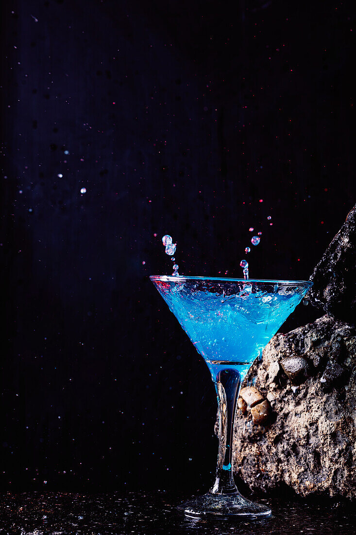 Glas mit alkoholischem Cocktail "Blaue Lagune" auf rauem Stein in hellem Studio