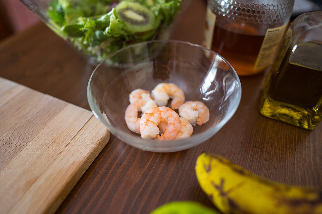 Von oben: Frische Shrimps in einer Glasschüssel neben Kochzutaten auf einem Küchentisch