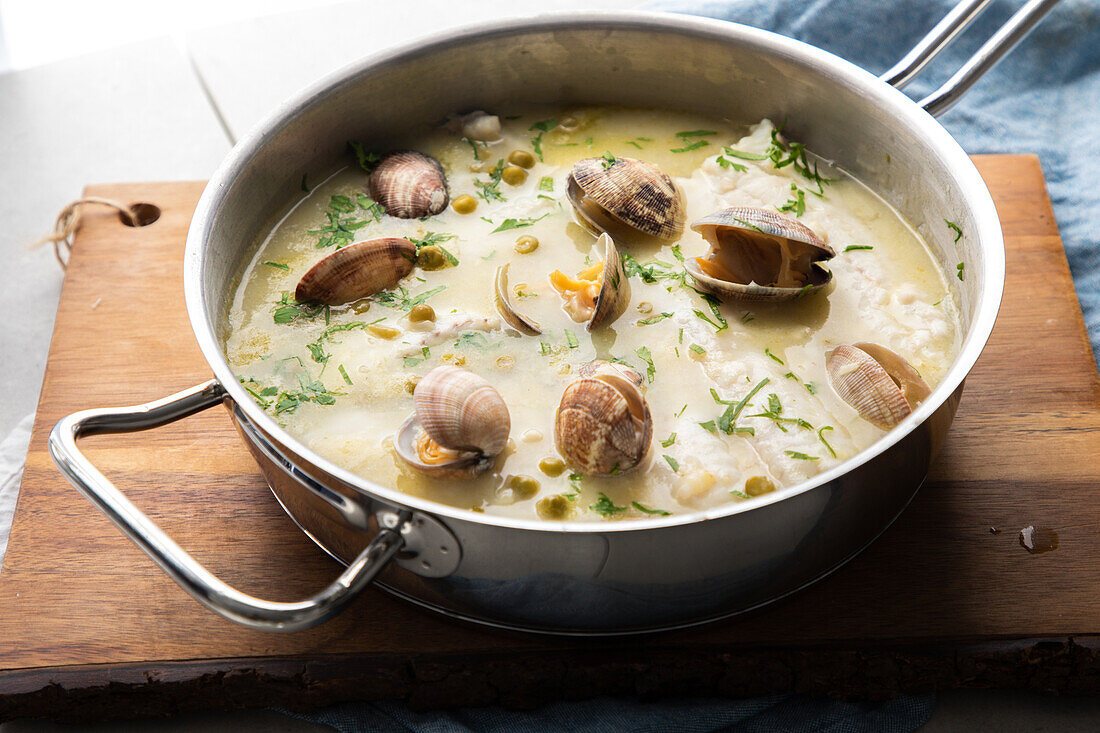 Von oben Metalltopf mit köstlicher Meeresfrüchtesuppe mit Venusmuscheln und Seehecht auf einem Holzbrett in der Küche