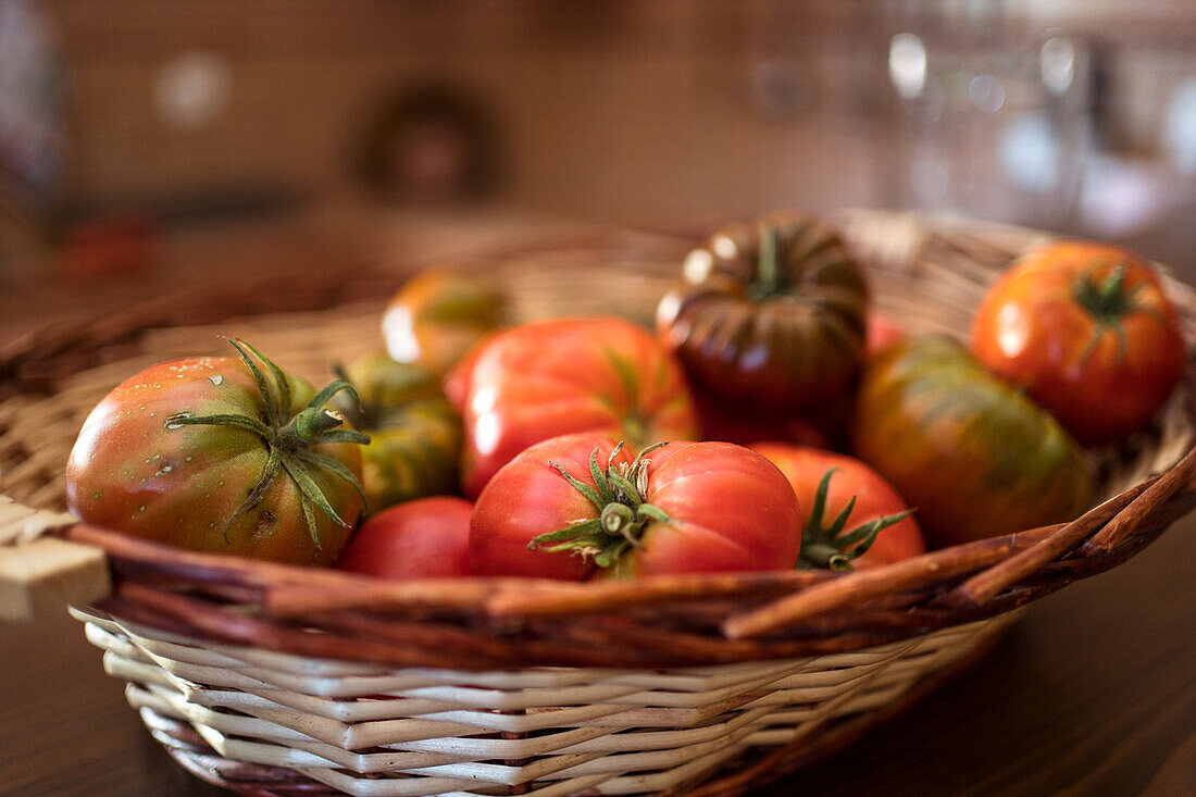 Pile of fresh tomatoes in wicker basket placed on table in rustic kitchen in harvest season
