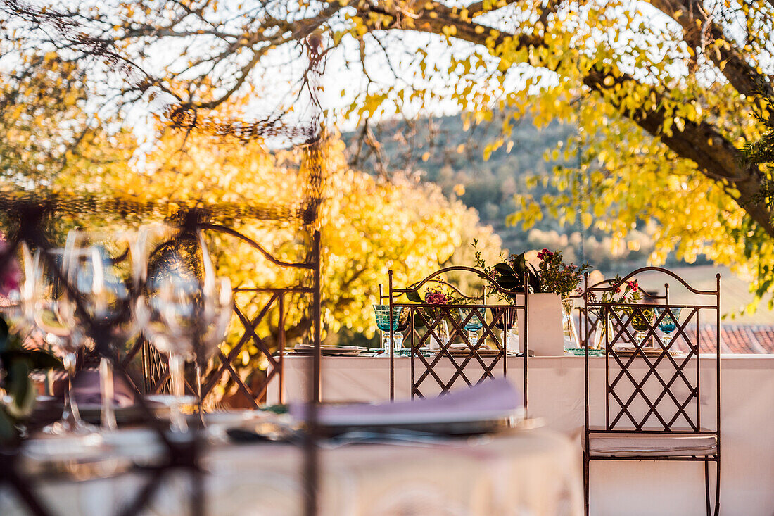 Geräumige Veranda mit Tellern, Weingläsern und Besteck auf mit frischen Blumen geschmückten Tischen für eine Hochzeitsfeier