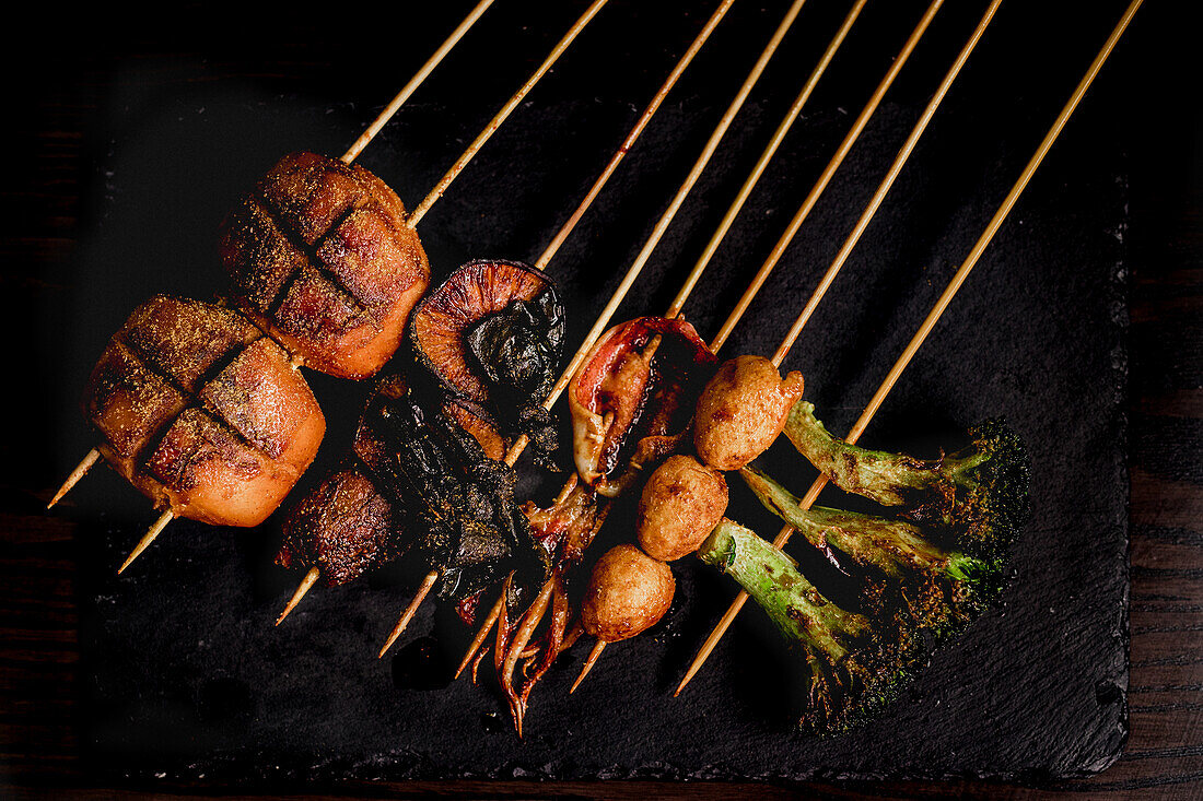 From above composition of tasty grilled skewers with meat, fish, squid and broccoli in cafe