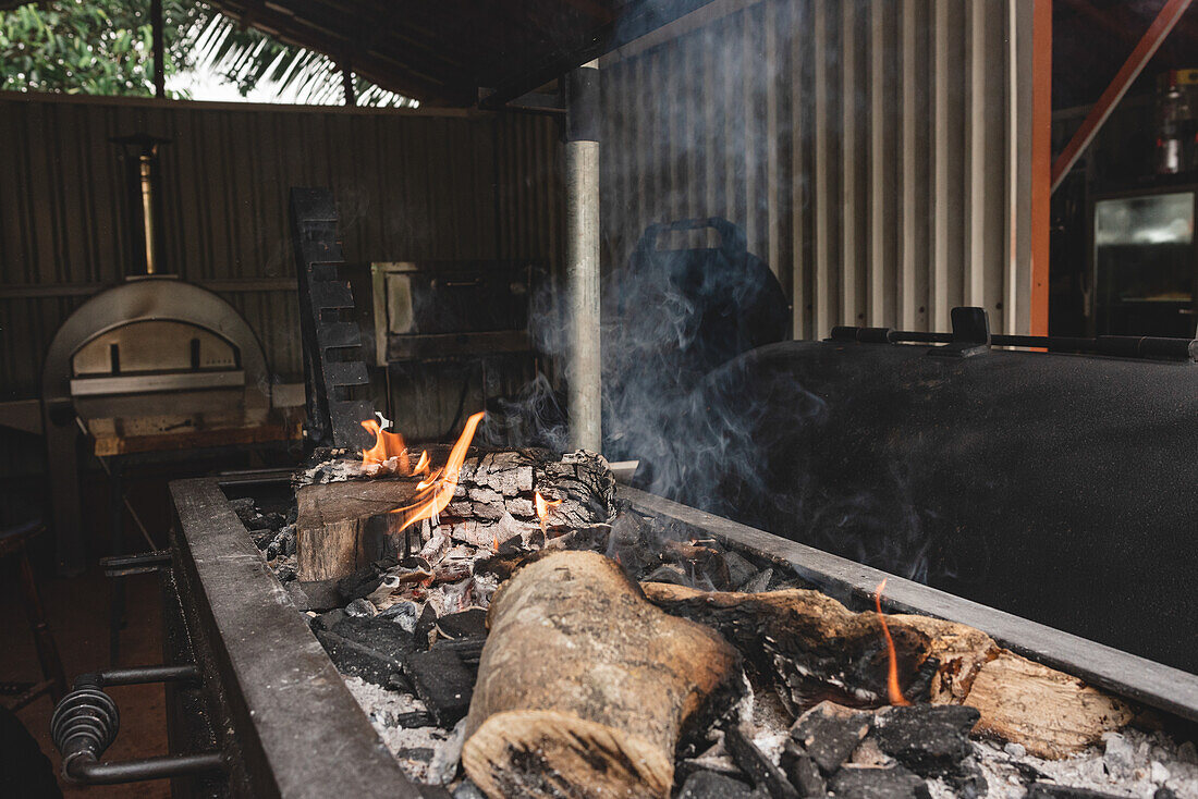 Heißes brennendes Holz in einem schwarzen Kohlenbecken mit Flammen und Kohle neben einem modernen Grill auf der Terrasse eines Cafés mit Mauern