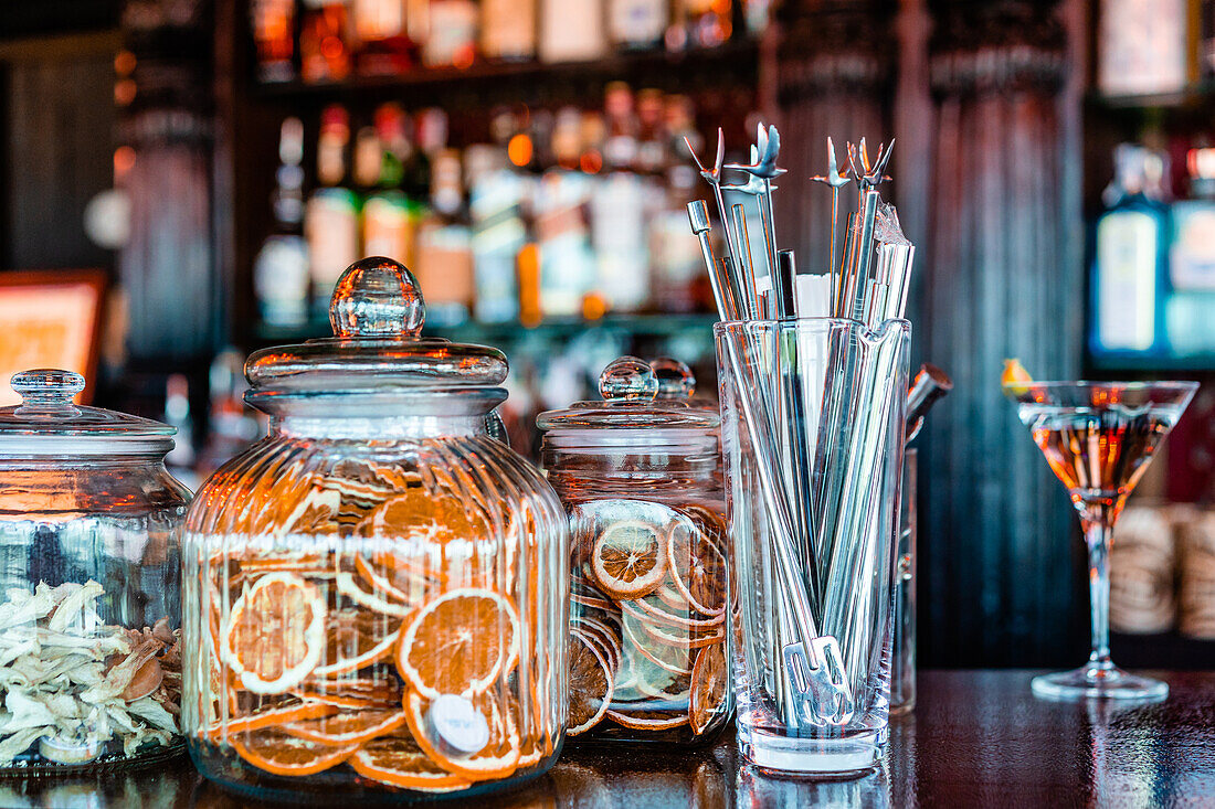 Barkeeper Metallwerkzeuge in Glas und verschiedene Dekorationen in Gläsern auf Holztheke im Pub