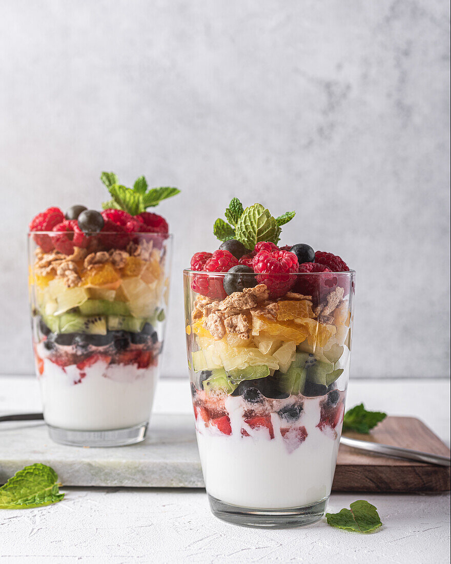 Appetitlicher Joghurt mit Schichten von frischen Früchten, serviert in Gläsern auf einem Tisch mit Minzblättern