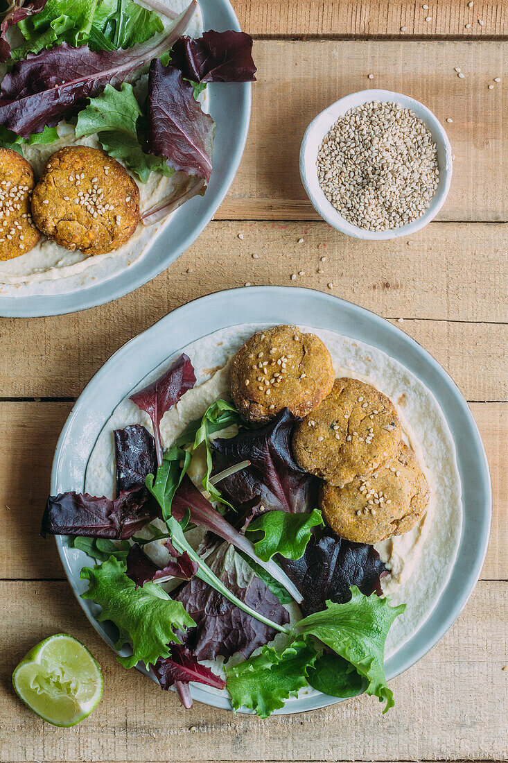 Teller mit frischem Salat und Süßkartoffel-Falafel neben Soße und Sesam auf Holztisch